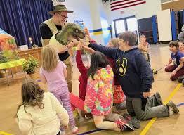 presenter holding t-rex dino puppet surrounded by children